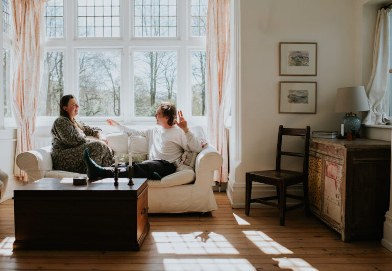 Two young people discuss life on a sofa by a sunny window